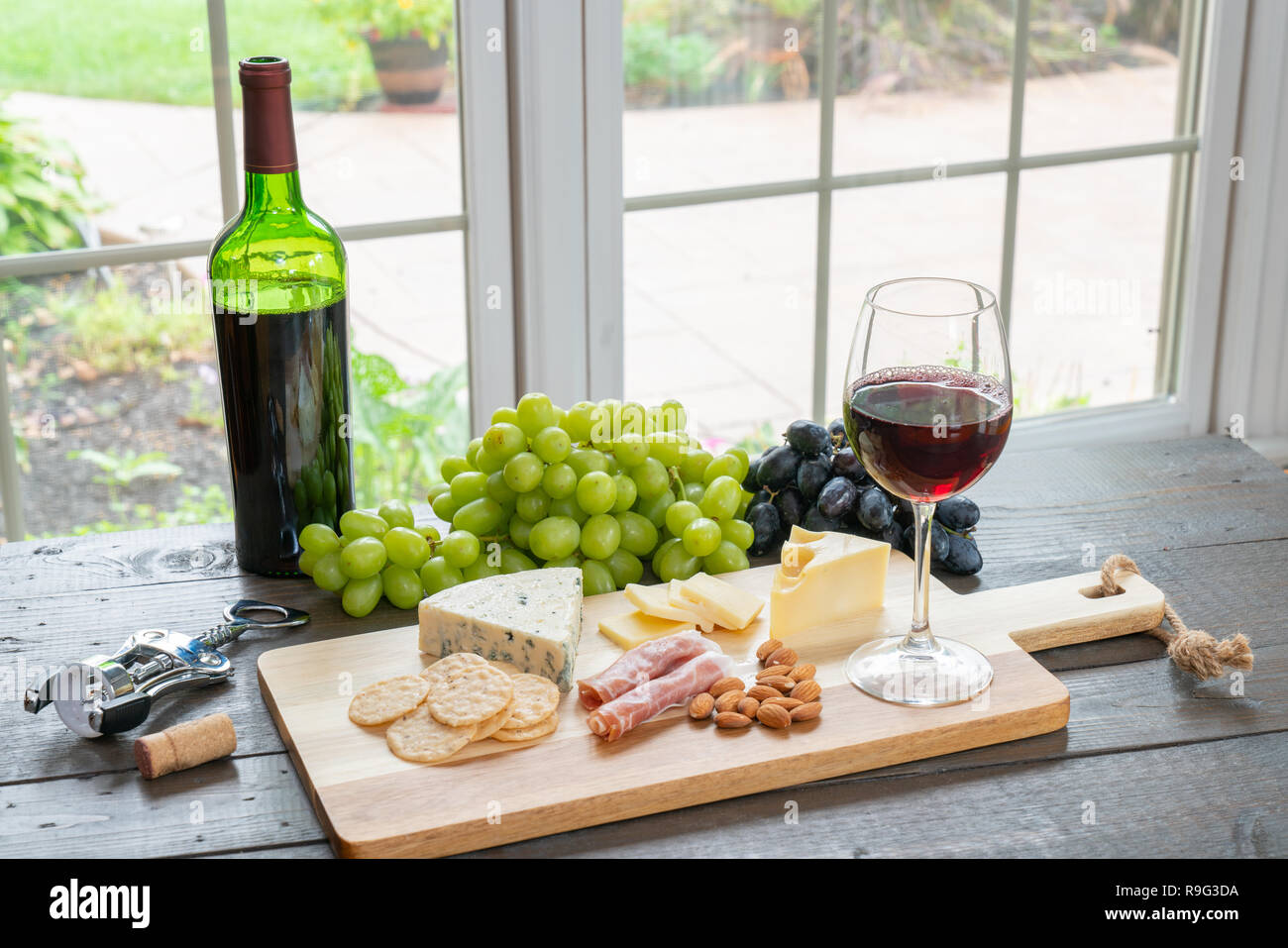 Bicchiere di vino rosso con bottiglia di vino, formaggio, cracker, mandorle e uva Foto Stock