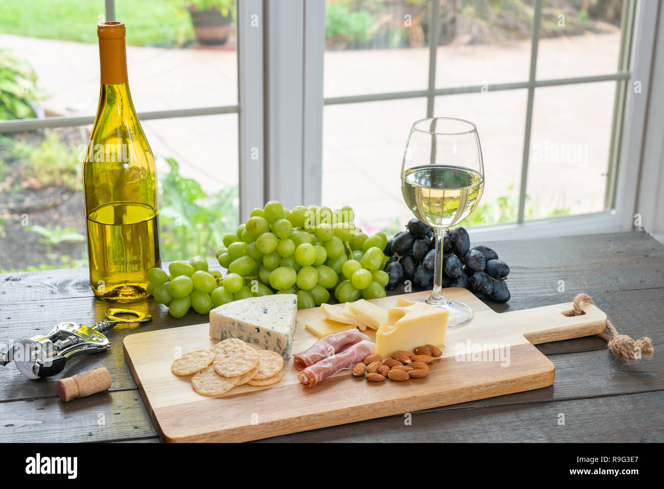 Bicchiere di vino bianco con bottiglia di vino, formaggio, cracker, mandorle e uva Foto Stock