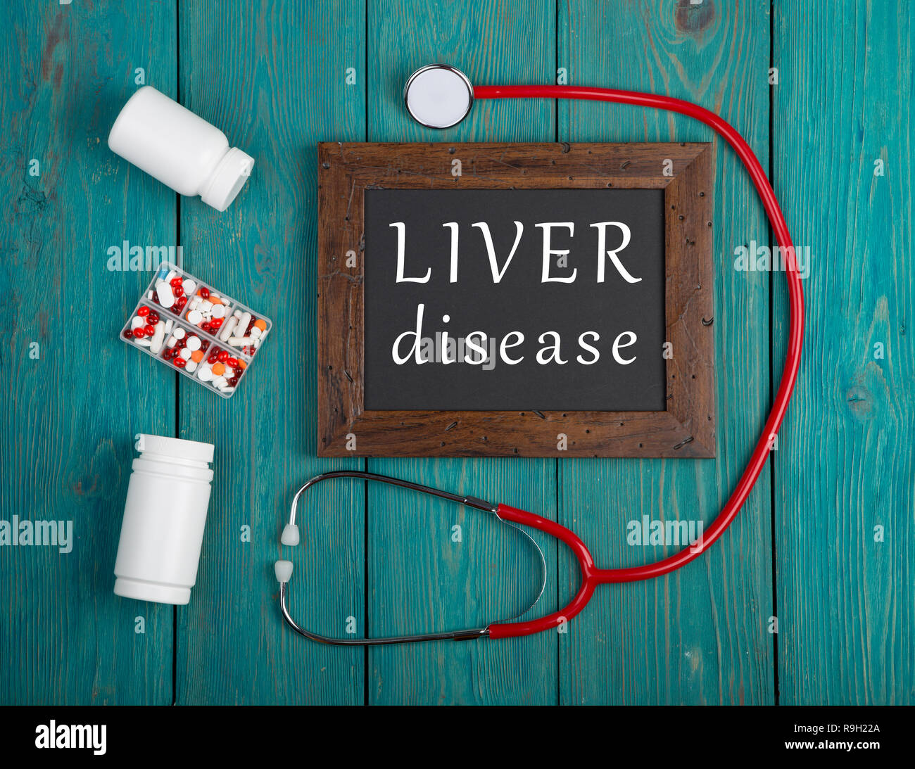 Concetto di medicina - Lavagna con il testo "malattia del fegato', pillole e stetoscopio blu su sfondo di legno Foto Stock