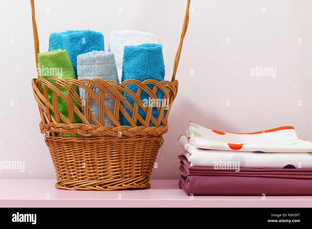 Sul comò vi è una pila di pulire stirare la biancheria da letto e vi è un cestello in rotoli o in fogli piegati asciugamani multicolore. Foto Stock