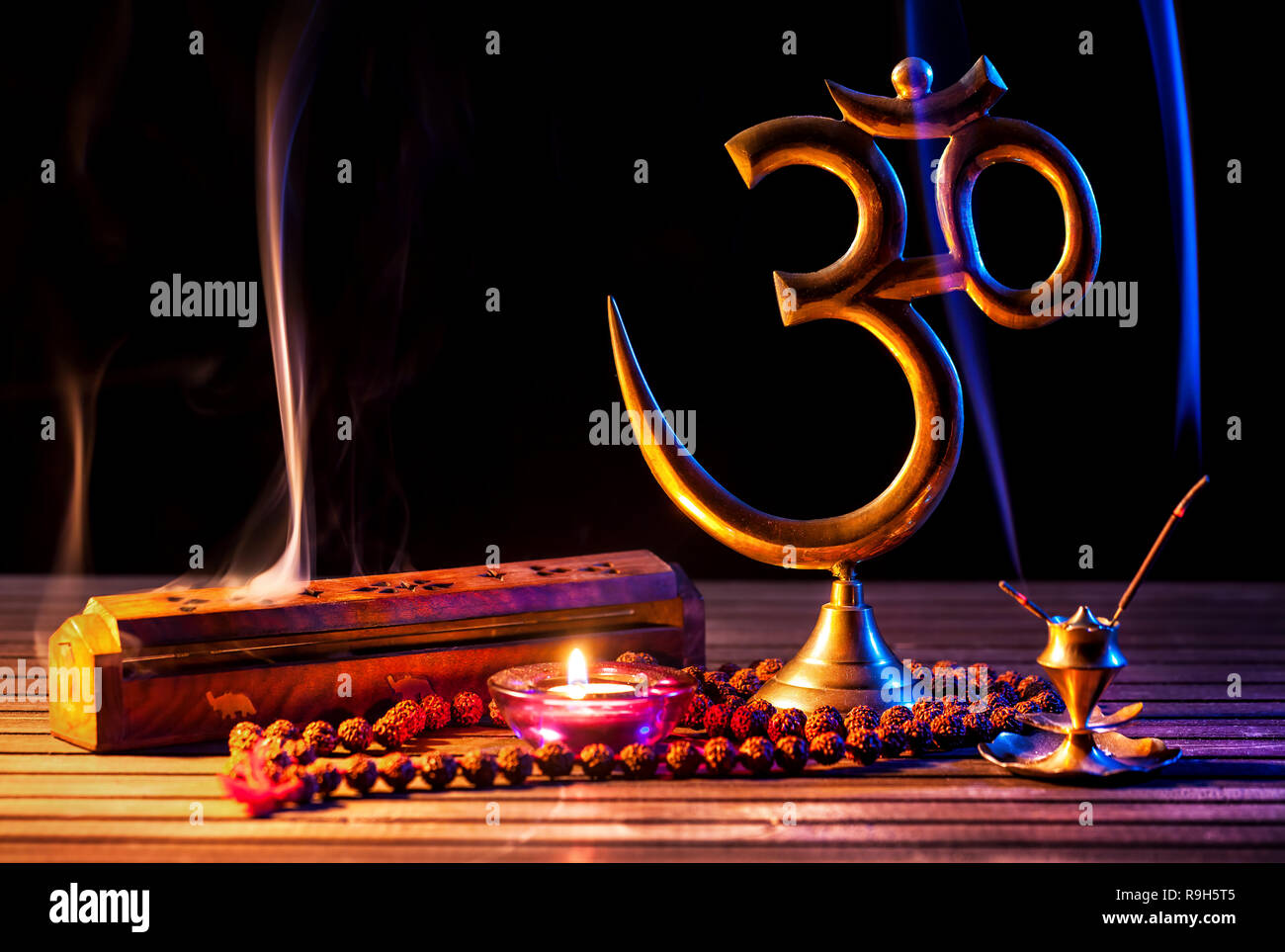 Om simbolo, incenso, fumo di candela e japa mala sul tavolo di legno a sfondo nero Foto Stock