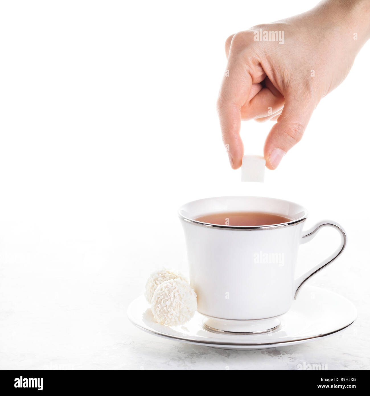 Donna mettendo mano lo zucchero nel tè nero in tazza bianca con due dolci palline di cocco bianco su sfondo marmo Foto Stock