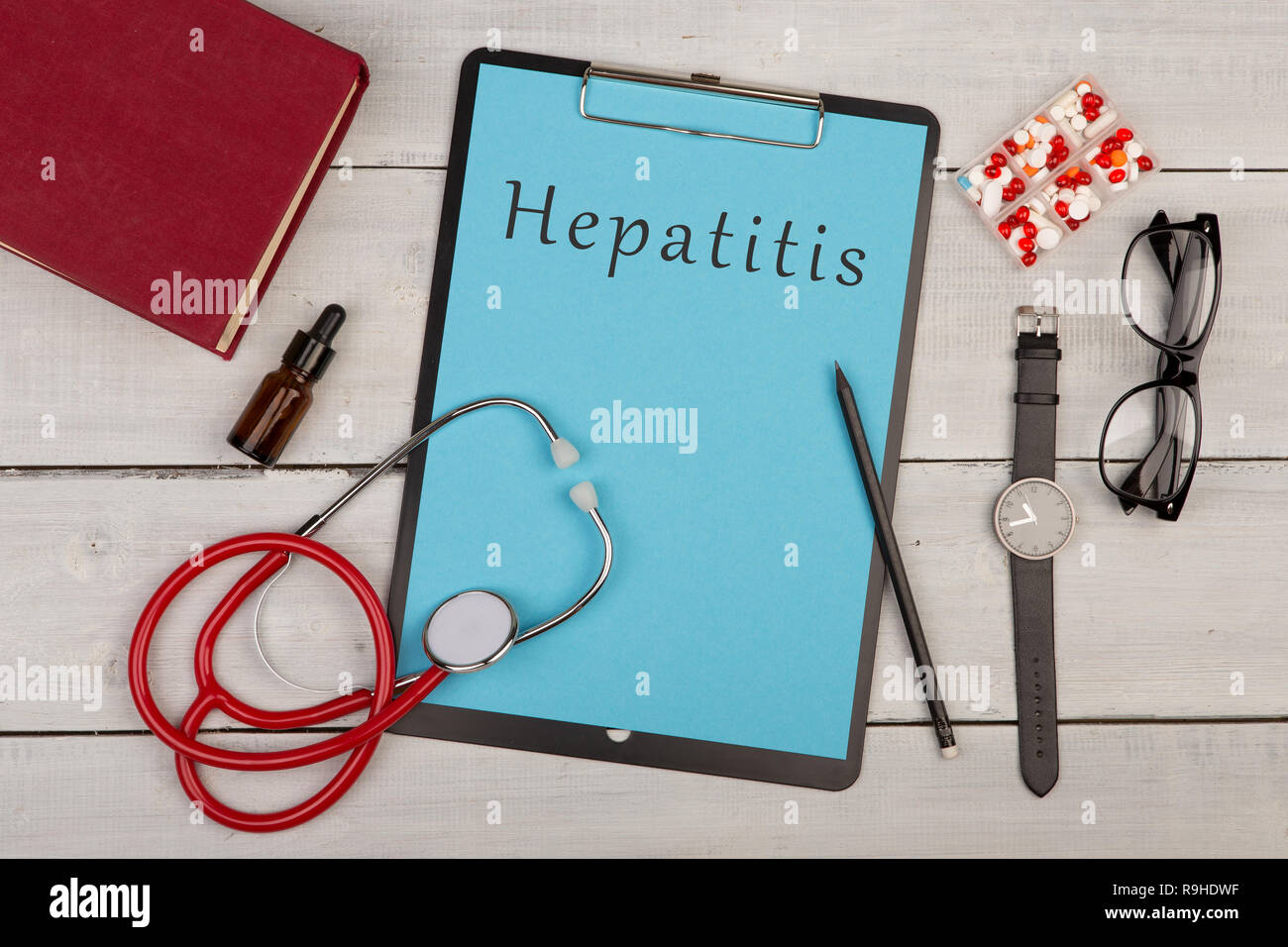 Concetto di medicina - clipboard con il testo "epatite', pillole, libro, occhiali, guardare e stetoscopio bianco su sfondo di legno Foto Stock