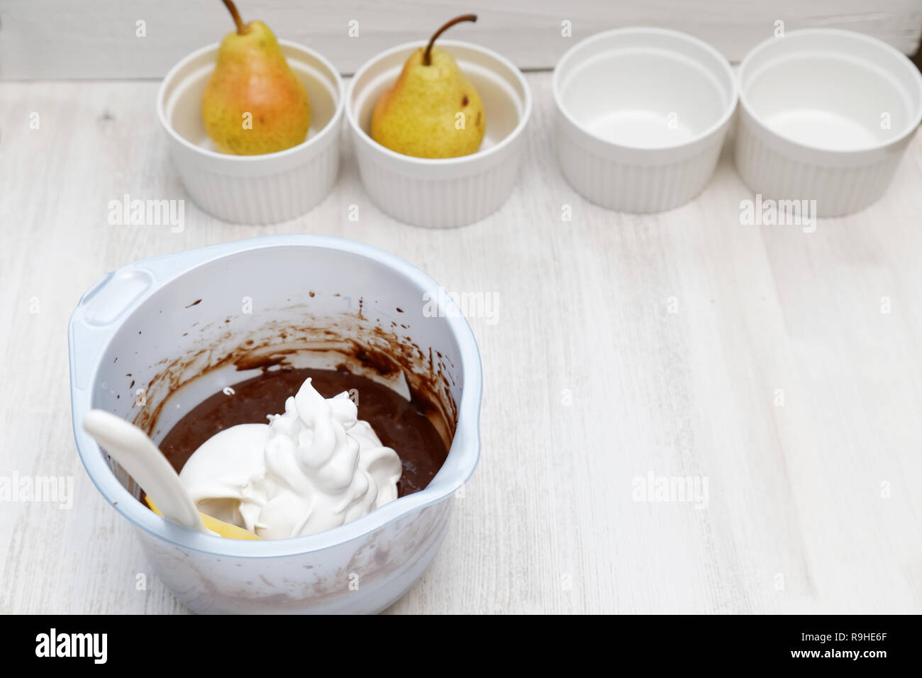 Ciotola con la panna montata e la pasta per il cioccolato-mandorla dolce bianco su un tavolo di legno. Ceramica piatto da forno e due materie pera matura in background. Foto Stock