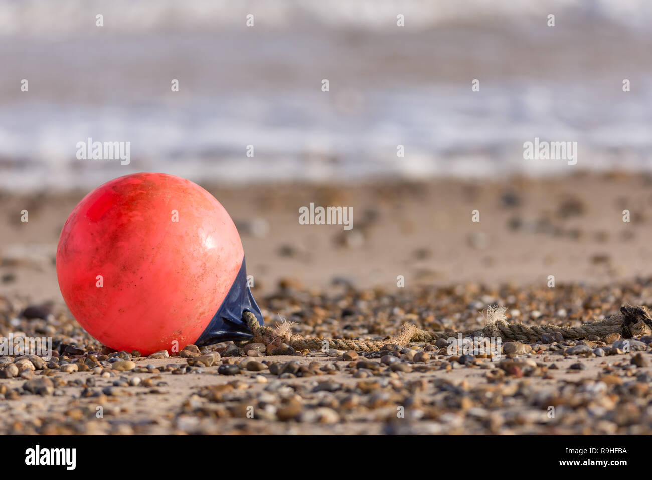 Boa arancione abbandonati sulla sabbia ghiaiosa spiaggia con piccole onde in background Foto Stock