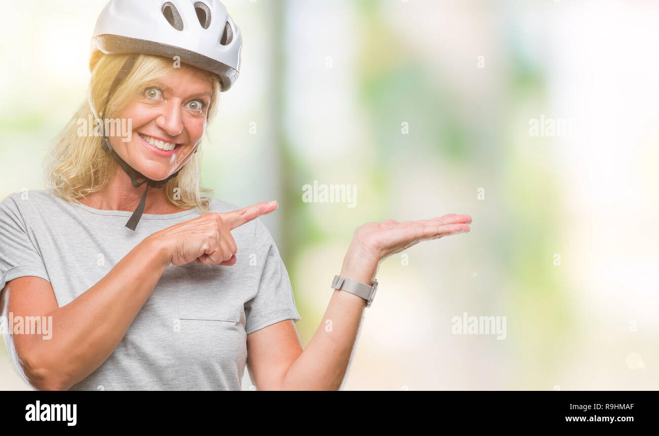 La mezza età caucasian ciclista donna che indossa il casco di sicurezza su sfondo isolato stupiti e sorridente alla fotocamera durante la presentazione con la mano e puntare Foto Stock