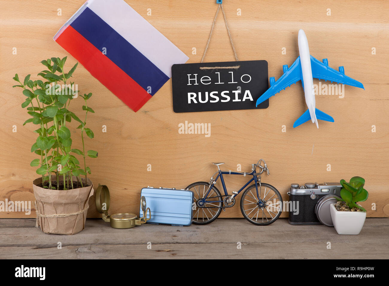 Il tempo di viaggio concetto - Lavagna con il testo "Hello Russia", Bandiera della Russia, fotocamera, modello di aeroplano, poco in bicicletta e in valigia, bussola su legno Foto Stock
