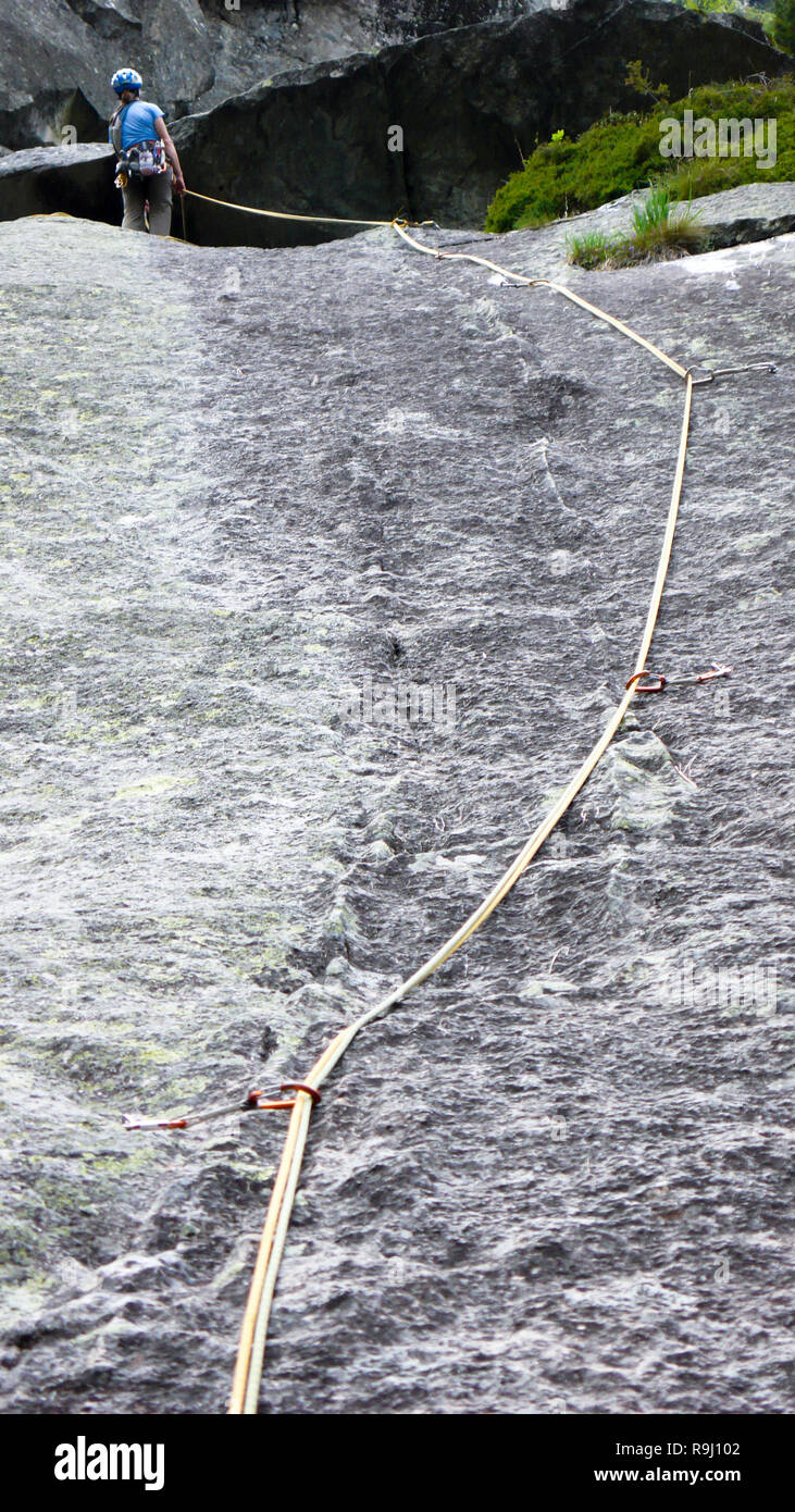 Female Rock scalatore in un atteggiamento di assicurazione con corda di arrampicata sulla verticale di una lastra di granito di arrampicata Foto Stock