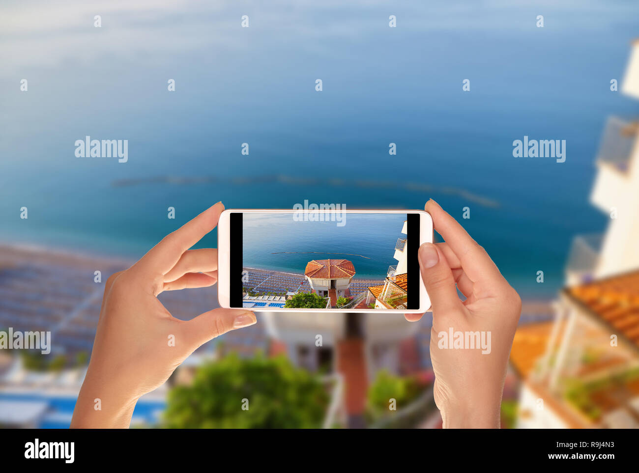 Un turista è scattare una foto della spiaggia sulla costa amalfitana con sedie a sdraio e ombrelloni su un telefono cellulare Foto Stock