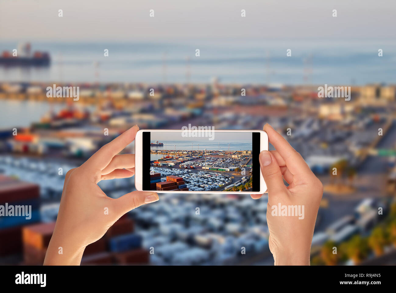 Un turista è scattare una foto del terminale della porta con contenitori, nuove vetture e vagoni nelle prime ore del mattino su un telefono cellulare Foto Stock