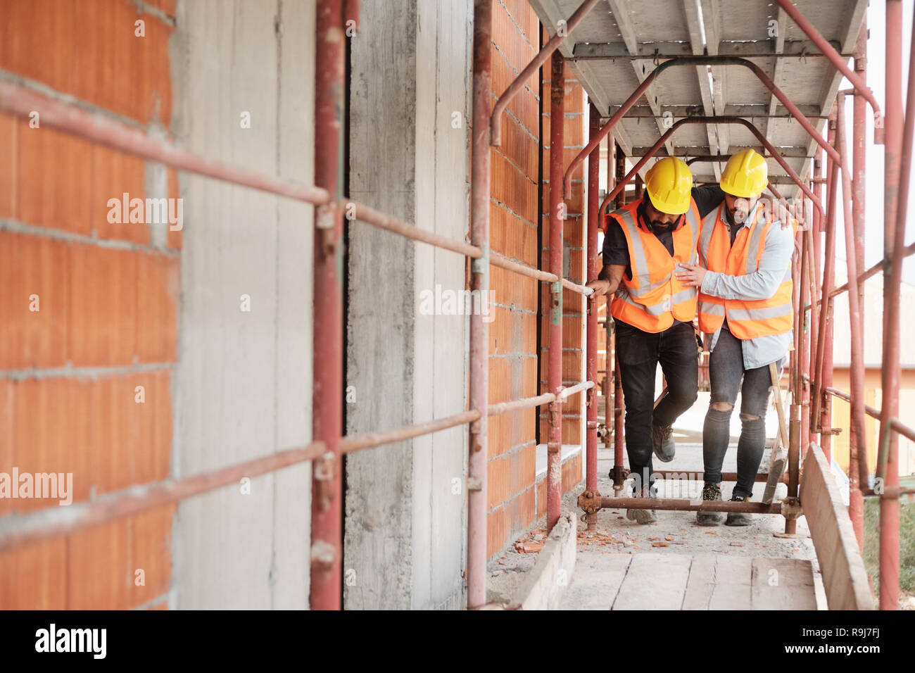 Le persone che lavorano nel sito in costruzione. Giovani uomini al lavoro in casa nuova all'interno di un condominio. Latino lavoratore manuale aiutando feriti co-lavoratore dopo ac Foto Stock