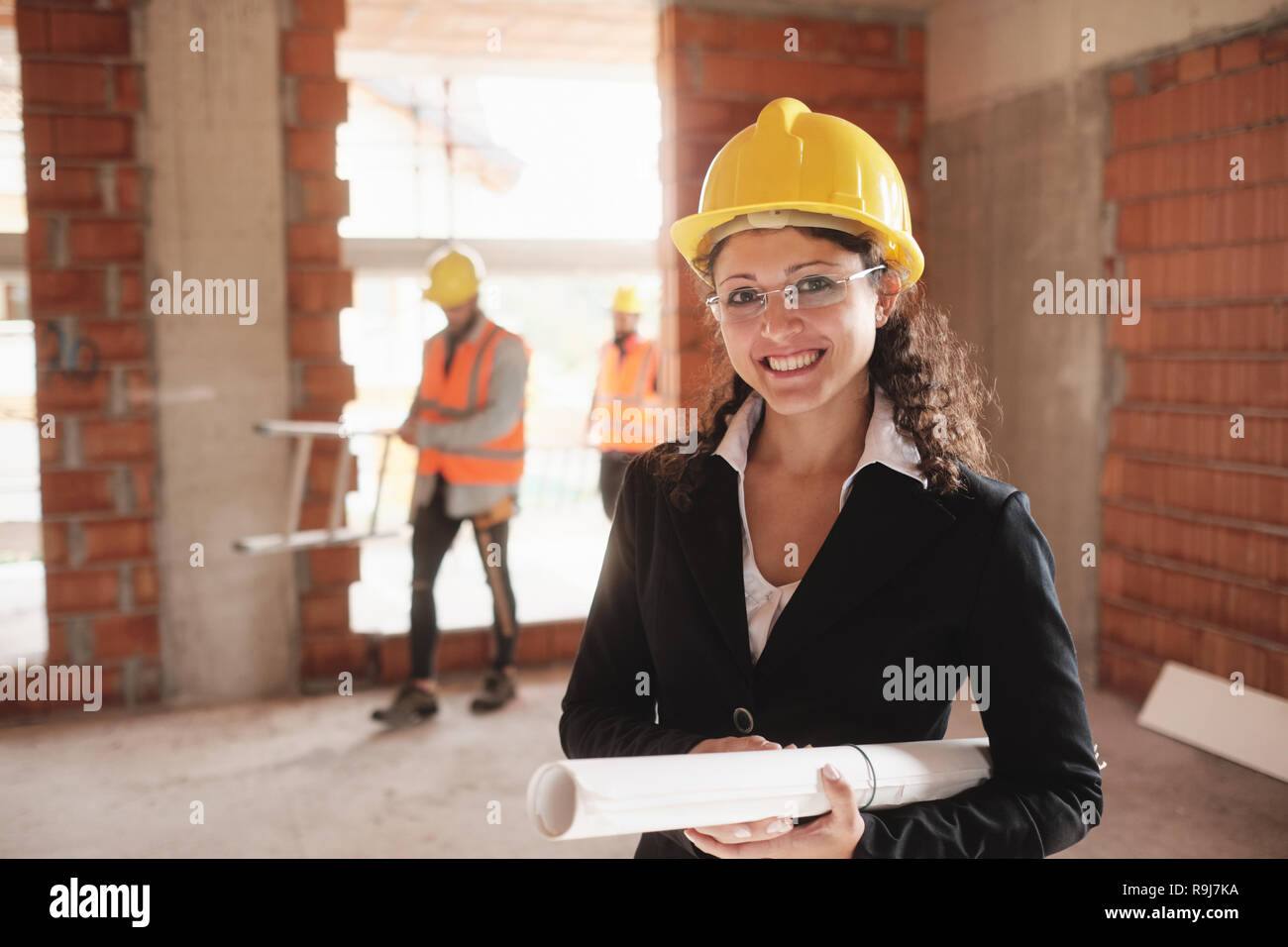 Donna con muratori nel nuovo edificio di appartamenti. Gruppo di operai al lavoro in casa e ritratto di felice architetto femmina. Forewoman guardando e sorridendo a Foto Stock