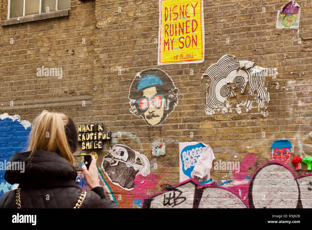 Una donna di scattare una foto con il suo iPhone di graffiti su Brick Lane, East London Foto Stock