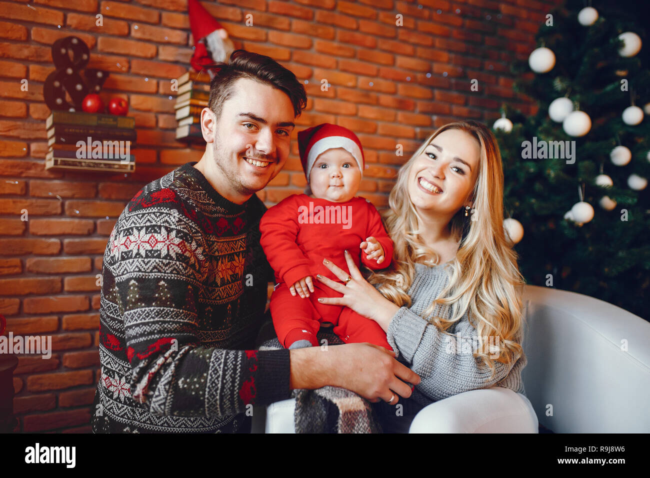 Bella famiglia seduta vicino ad albero di Natale. Carino madre in un maglione grigio. Ragazzino con bello padre Foto Stock