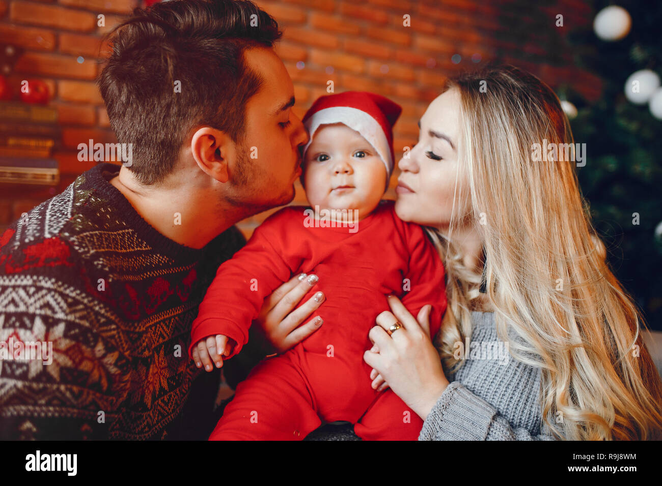 Bella famiglia seduta vicino ad albero di Natale. Carino madre in un maglione grigio. Ragazzino con bello padre Foto Stock