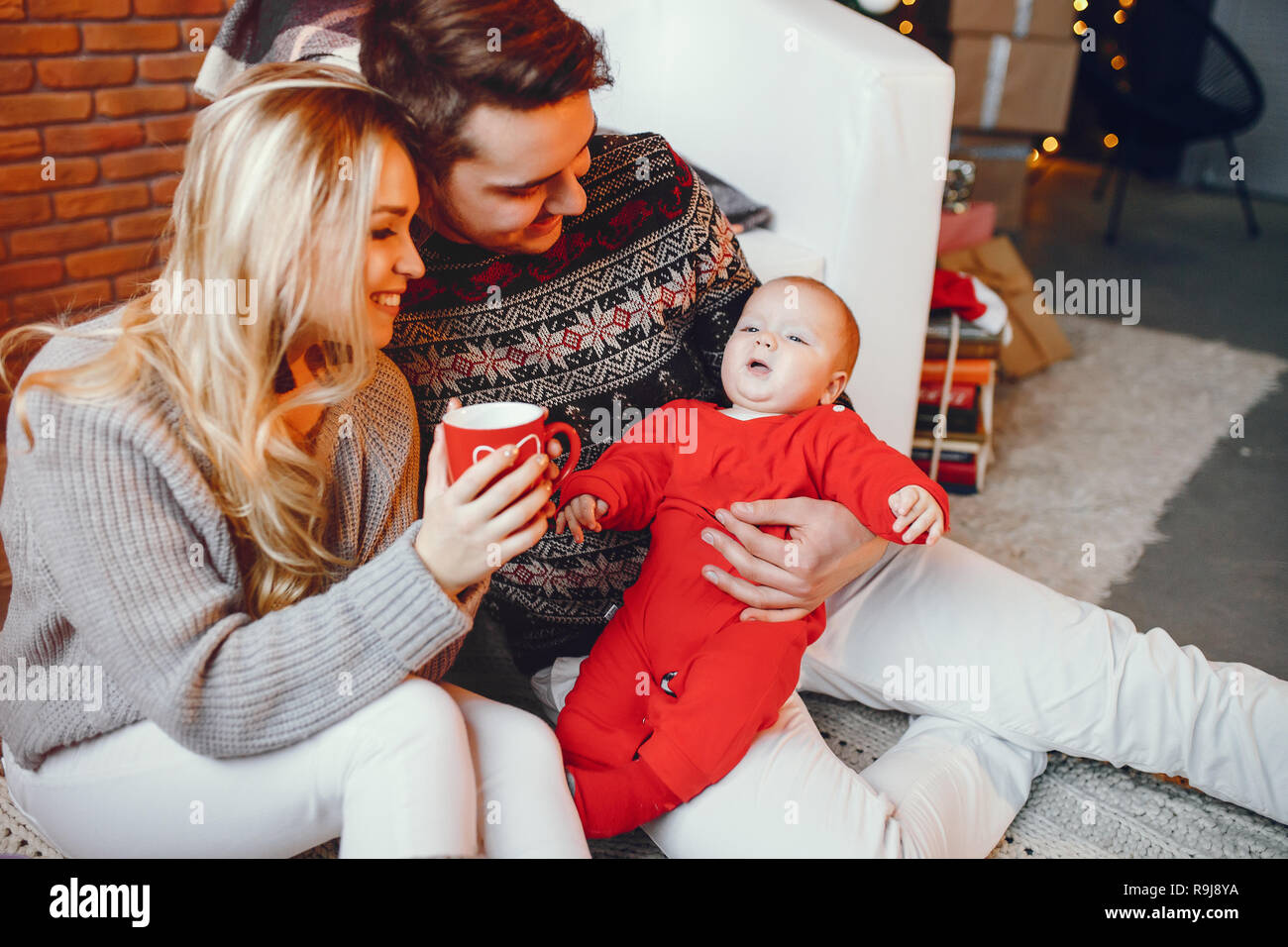 Bella famiglia seduta vicino ad albero di Natale. Carino madre in un maglione grigio. Ragazzino con bello padre Foto Stock