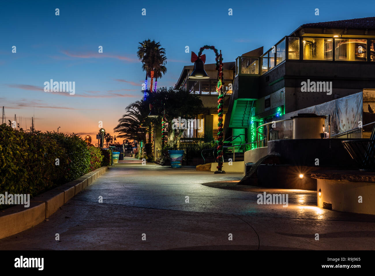 Le luci di Natale avvolto intorno alle lampade e palme sotto alba cielo lungo Ventura Harbor negozi in California, Stati Uniti d'America il 24 dicembre 2018. Foto Stock