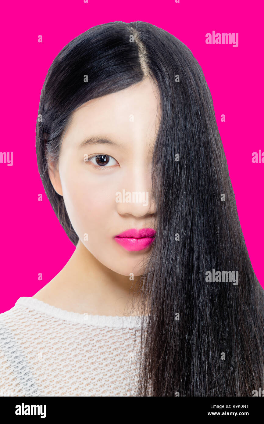 Adolescente americano asiatico ragazza con i capelli che copre metà faccia su sfondo rosa Foto Stock