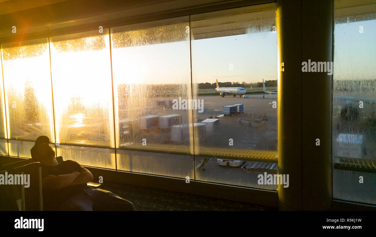 Sleeping traveler con Rising Sun in sparsly affollata terminale, l'Aeroporto Internazionale di Orlando, FL Foto Stock