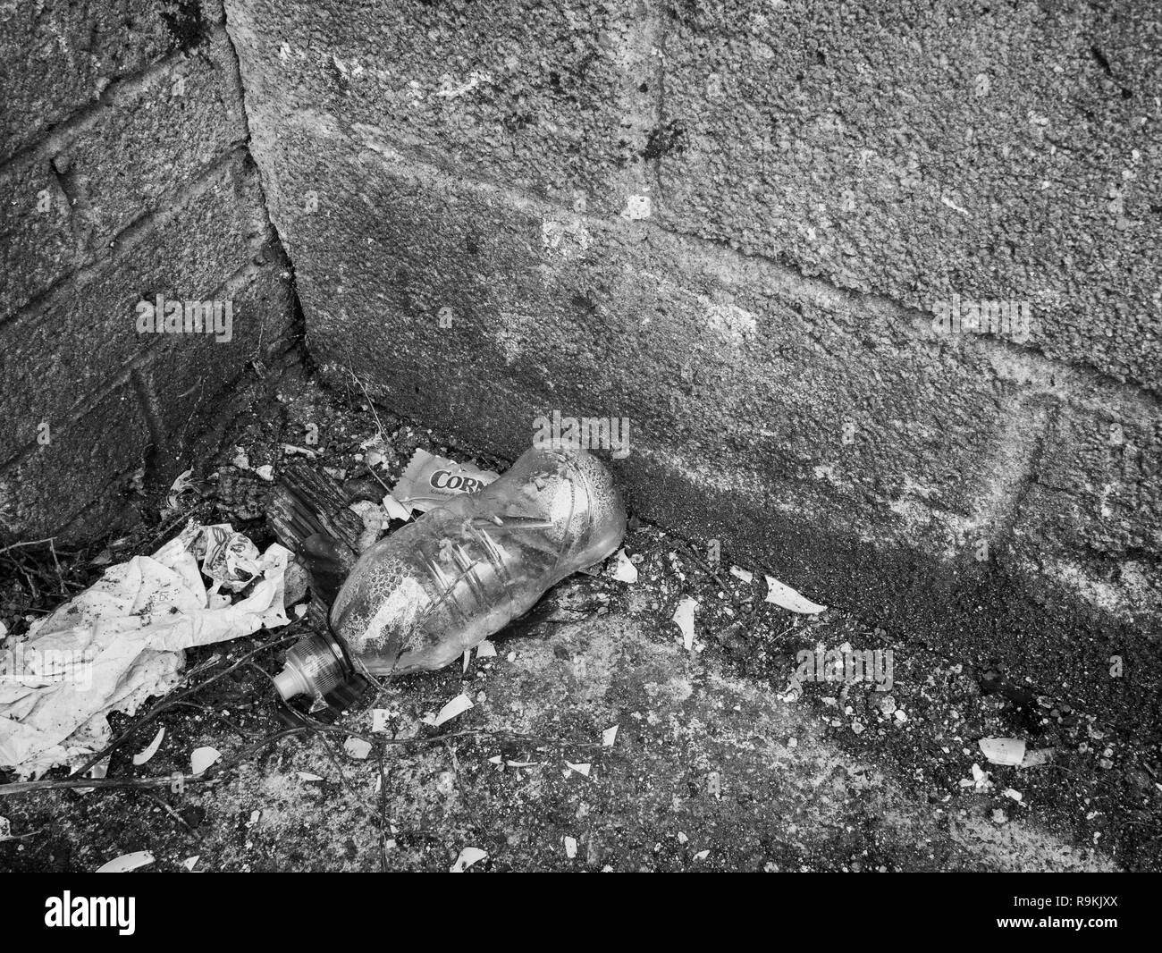 PTFE drink di plastica bottiglia scartato in ambiente urbano backstreet. Metafora di inquinamento in plastica, guerra sui rifiuti in plastica. Versione monocromatica di R9KJNW. Foto Stock