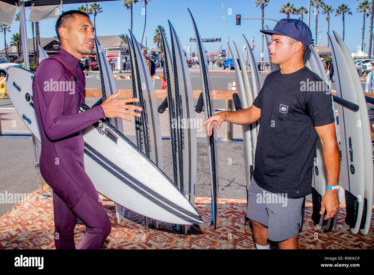 Un surfista in una muta discute i punti più delicati del suo sport con una tavola da surf venditore presso un display esterno al famoso molo a Huntington Beach, CA. Foto Stock