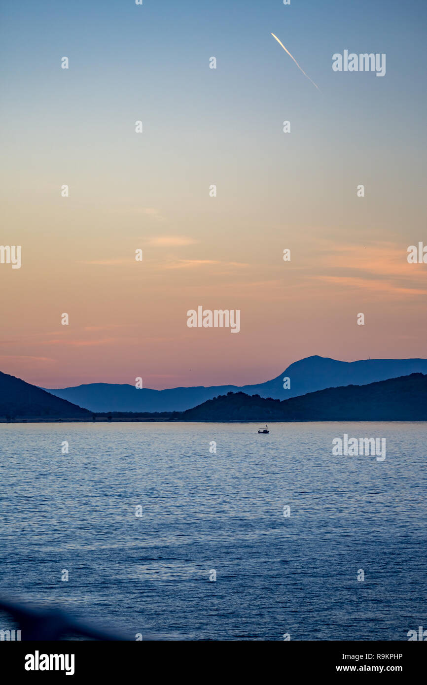 Scenario sunset seascape nel Mar Ionio con la gamma della montagna lontano e la sagoma di piccole barche da pesca, la foto è stata scattata nell'ora d'oro Foto Stock