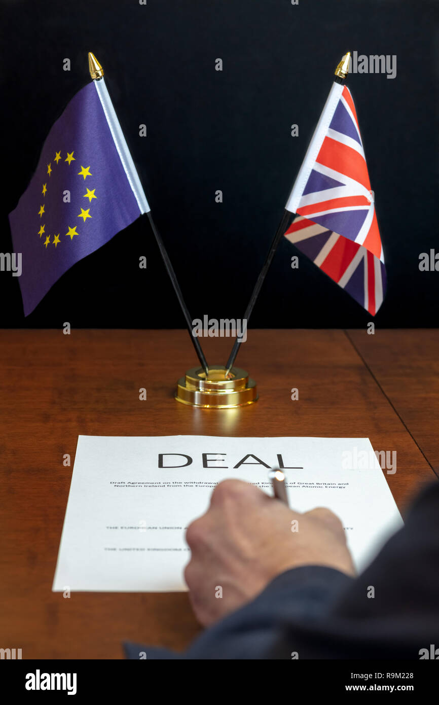 Concetto Brexit. Mano maschio dal retro firma foglio di carta intestata 'Deal' su una scrivania con piano di tavolo UK e UE bandiere dietro Foto Stock