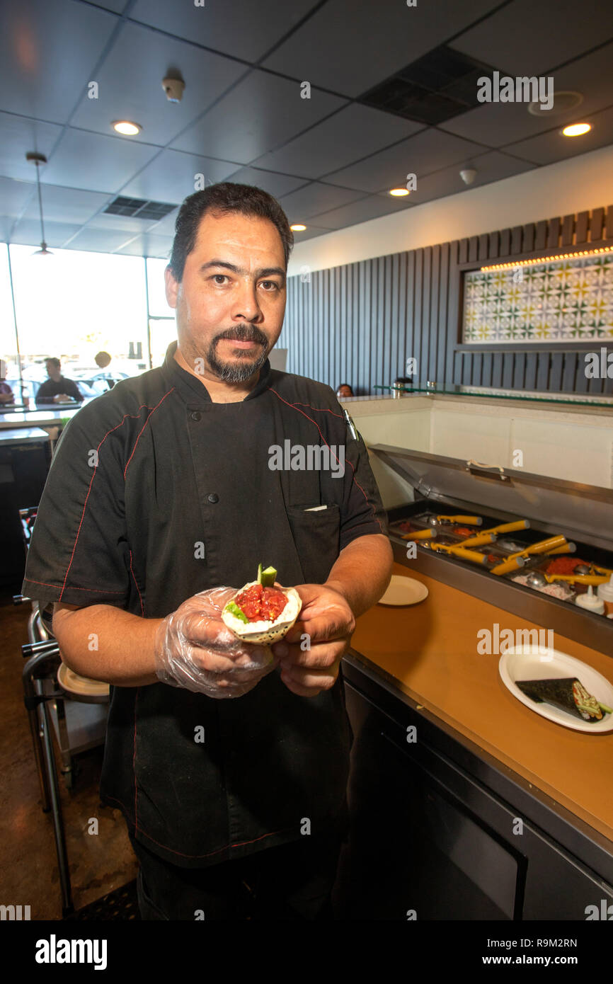 Utilizzando una varietà di ingredienti, un cuoco ispanica crea un rotolo di mano snack presso un ristorante giapponese in Costa Mesa, CA. Foto Stock