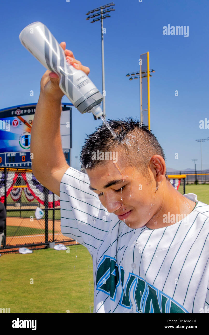 In un caldo pomeriggio estivo presso un Irvine, CA, softball stadium, un lettore in uniforme non si raffredda con uno spruzzo di acqua. Foto Stock