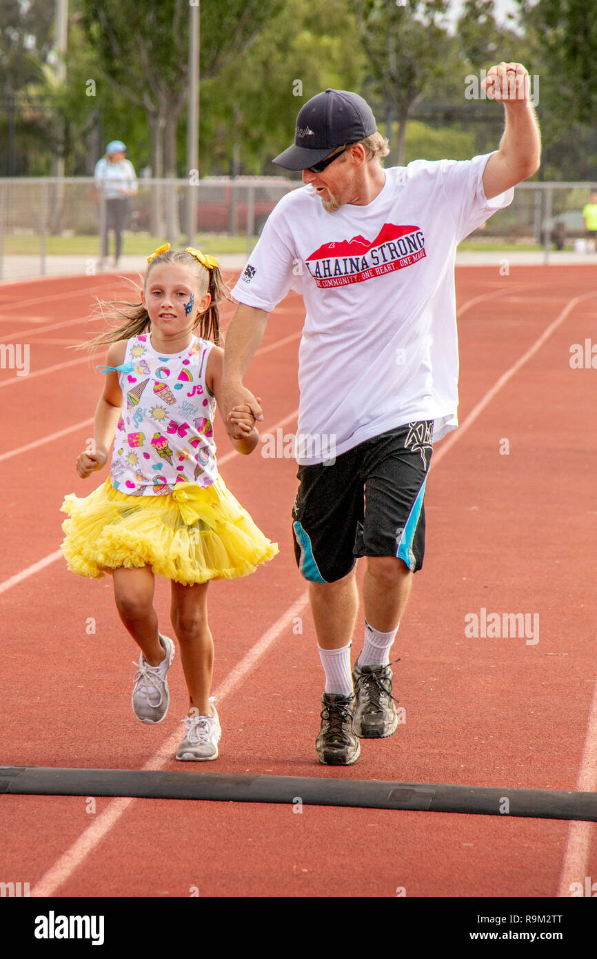 Un 9-anno-vecchia ragazza prende qualche incoraggiamento dal suo papà come essi attraversano il traguardo di una comunità il piede ad una gara di Costa Mesa, CA, stadium. Foto Stock