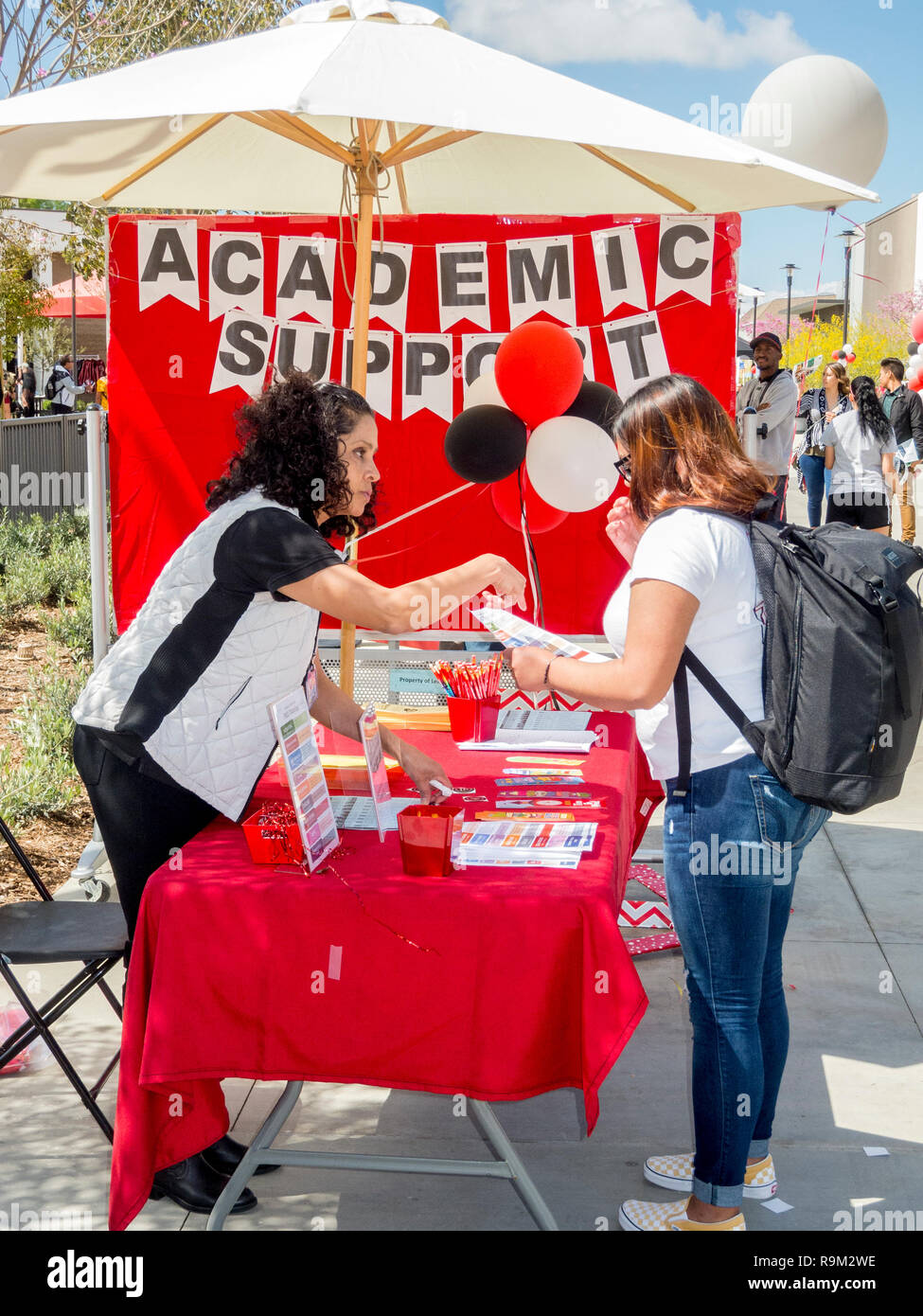 In un palloncino decorato outdoor community college campus tavola in Santa Ana CA, un insegnante spiega servizi accademici disponibili per una femmina ispanica studente. Foto Stock