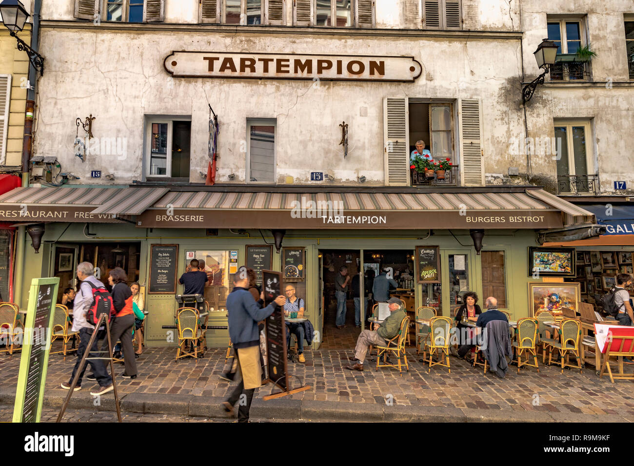 Un uomo che guarda fuori dalla finestra al piano superiore davanti alle persone sedute ai tavoli fuori dal Tartempion, un ristorante a Montmartre, Montmartre, Parigi, Francia Foto Stock