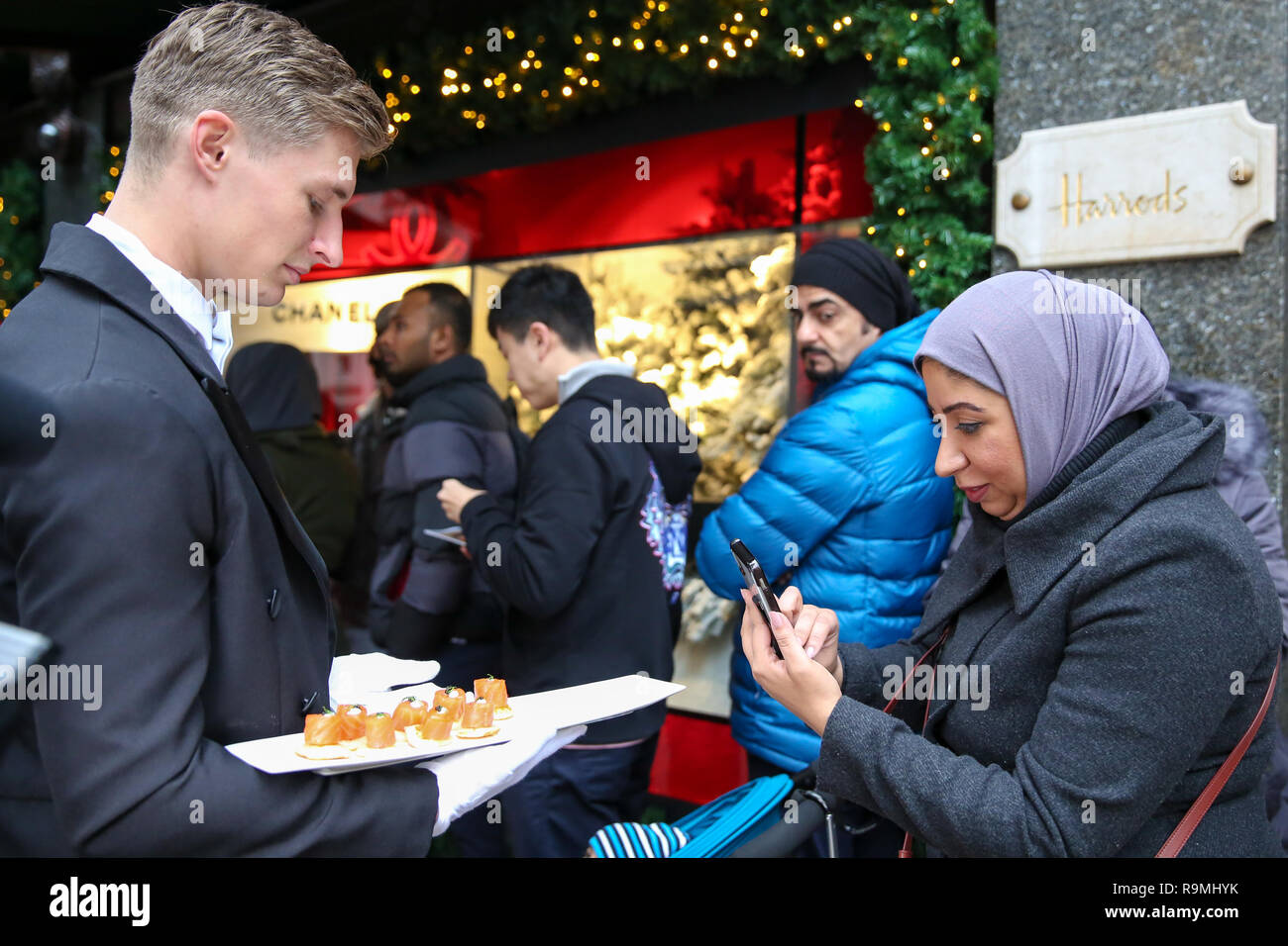 Harrods, Knightsbridge di Londra, Regno Unito. 26 dic 2018 - Gli acquirenti sono serviti con CanapŽ da Harrods butler come code di essi al di fuori del Luxury department store di Knightsbridge, davanti all'apertura del Boxing Day vendita. Boxing Day è uno dei giorni più impegnativi per i punti vendita al dettaglio con decine di migliaia di acquirenti approfittando del post-natale occasioni. Credito: Dinendra Haria/Alamy Live News Foto Stock