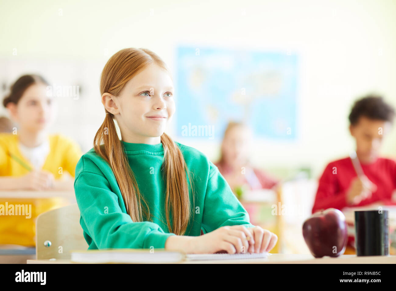 Contenuto redhead ragazza seduta alla scrivania a scuola Foto Stock