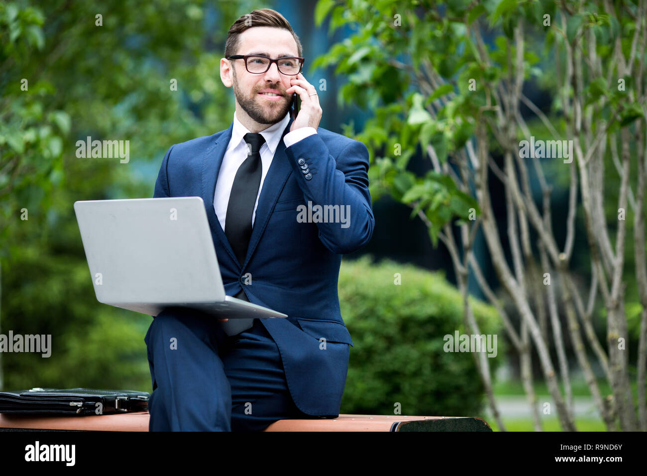 Business sorridente uomo seduto su un banco di lavoro con computer portatili e smartphone Foto Stock
