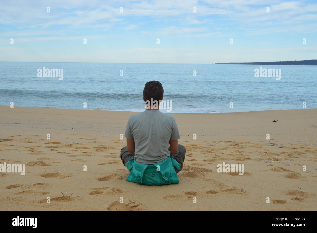 Uomo seduto cross gambe, guarda al mare, relax e pensando al mondo. Foto Stock