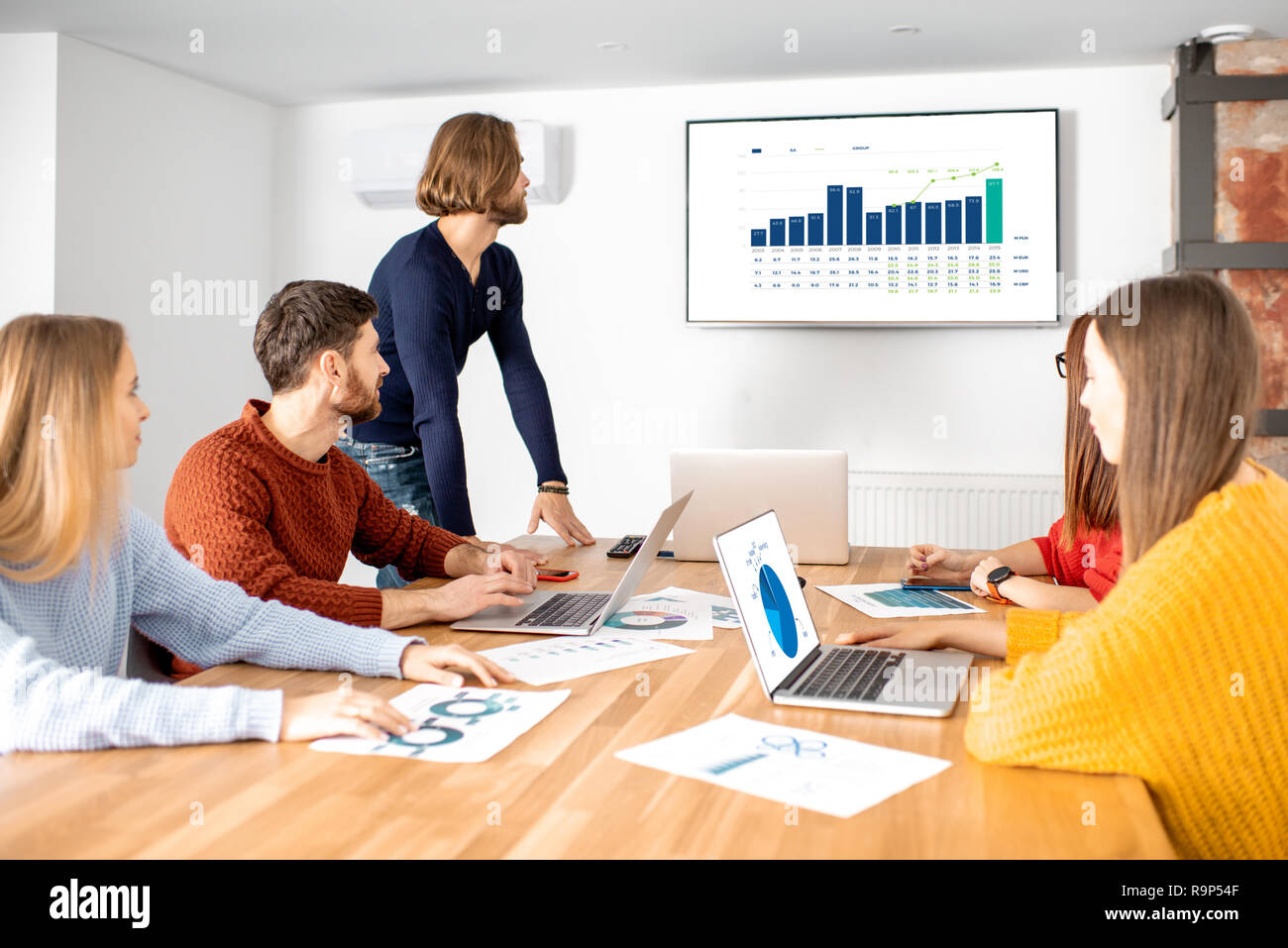 I colleghi vestito casualmente seduti insieme durante la riunione nella sala riunioni con alcuni grafici e statistiche Foto Stock