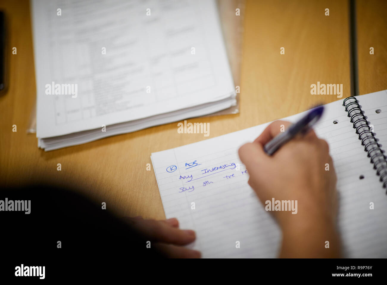 La scrittura di note in una nota scuola prenota linea Compiti di carta a una scrivania Foto Stock