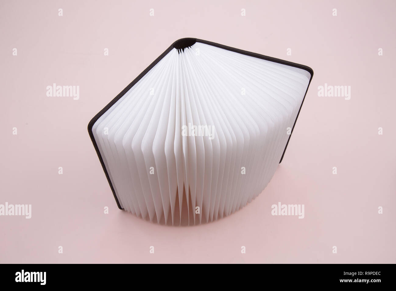 Un libro si sviluppa su un sfondo rosa Foto Stock