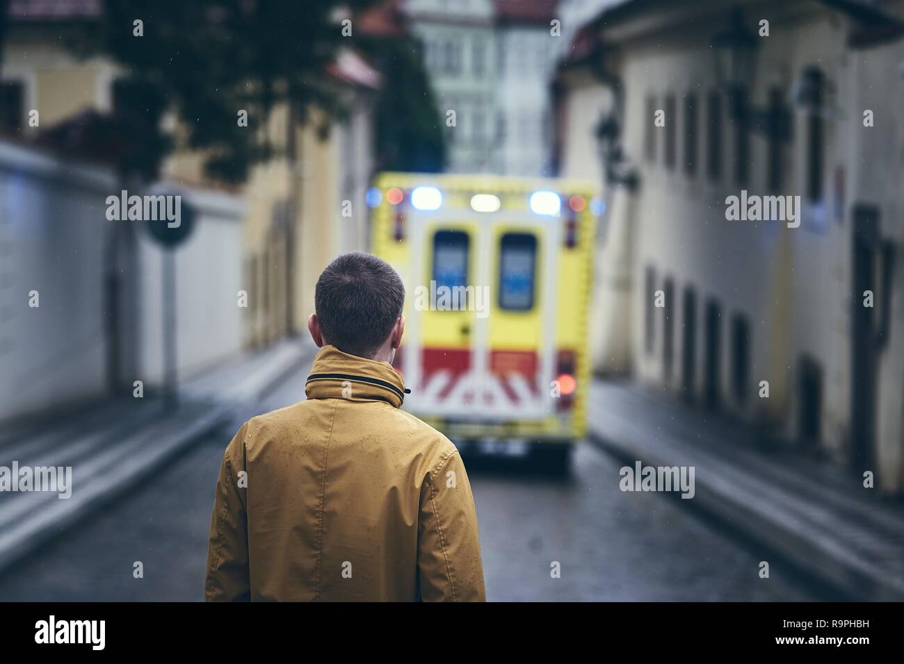 Uomo che guarda lasciando ambulanza del servizio di emergenza medica in giorno di pioggia. Concetti di salvataggio, di tristezza e di lasciare. Foto Stock