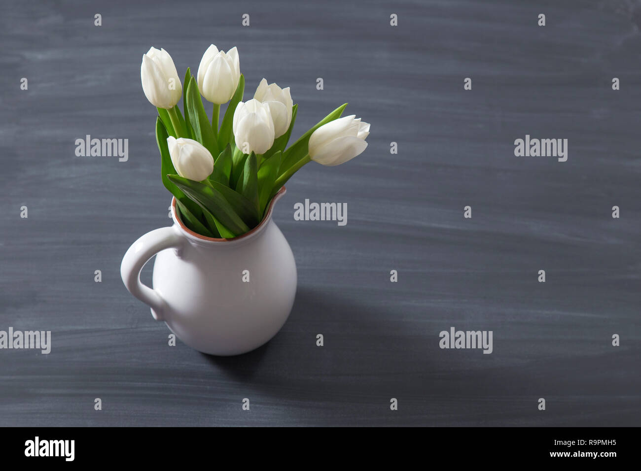 Bouquet di tulipani bianco in un rustico oldfashion vaso recipiente. Colore della luce Fiori a Caraffa del Bianco su sfondo lavagna. Foto Stock