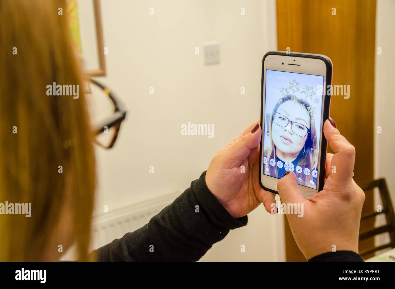 Una signora prende un selfie utilizzando Snapchat su un iPhone che migliora l'immagine con effetti Foto Stock