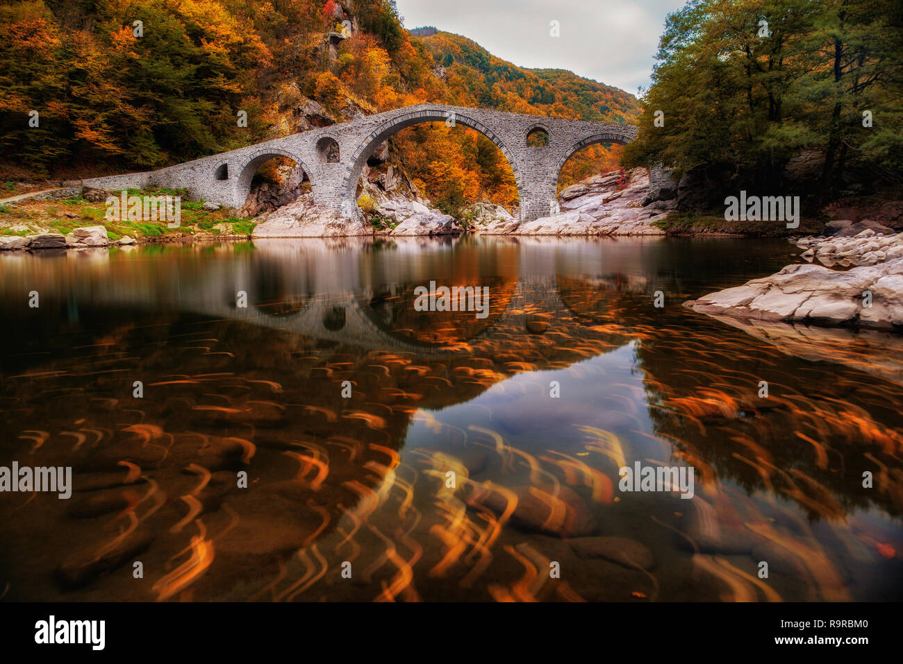 Ponte del Diavolo, Bulgaria. Antico ponte di pietra sul fiume Arda, tempo d'autunno con foglie in acqua. Sui monti Rodopi Foto Stock