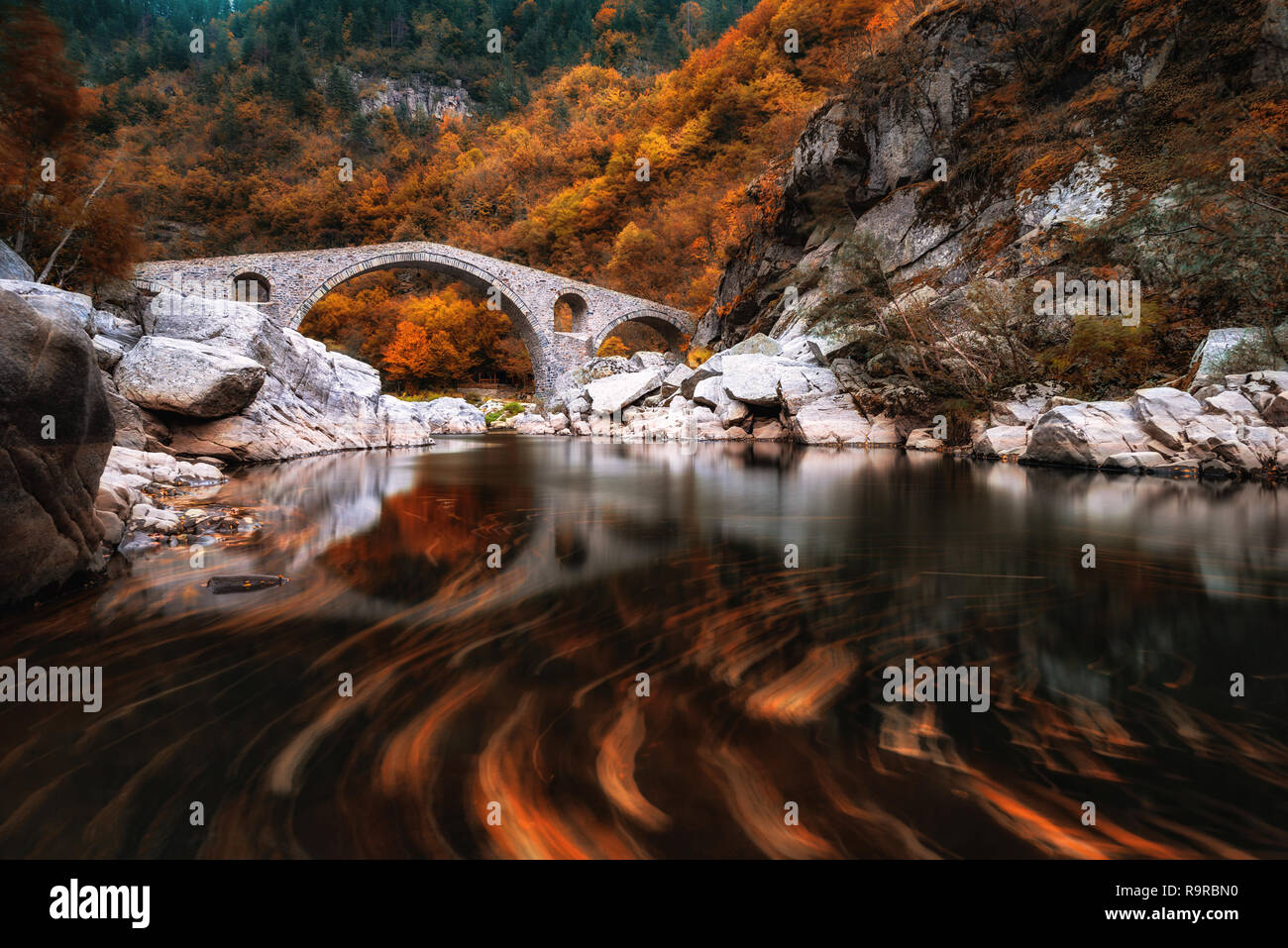 Ponte del Diavolo, Bulgaria. Antico ponte di pietra sul fiume Arda, tempo d'autunno con foglie in acqua. Sui monti Rodopi Foto Stock