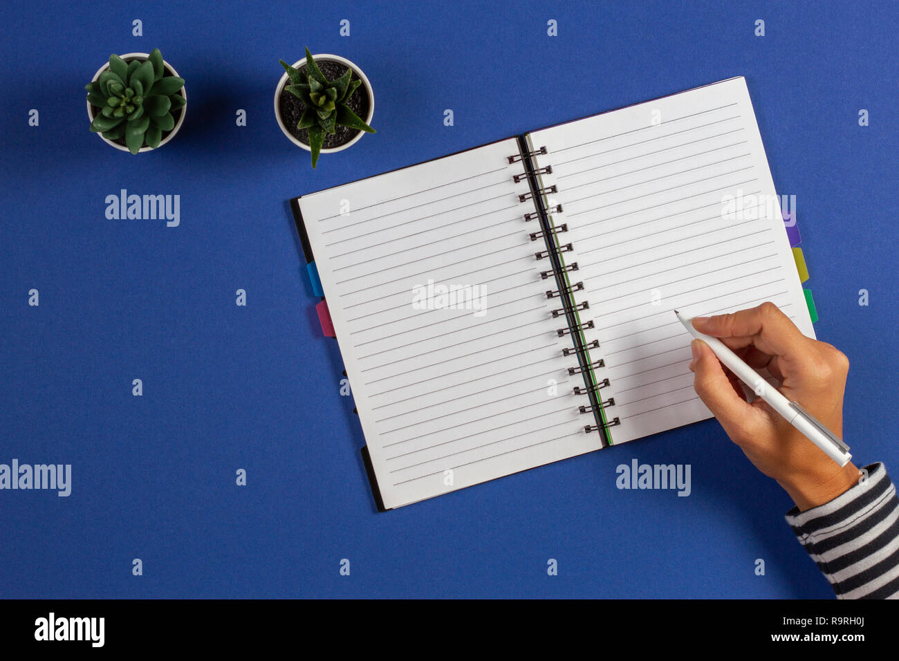 Ragazza la scrittura a mano con penna in notebook diario su sfondo blu. Foto Stock