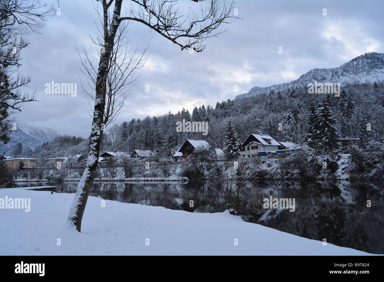 L'accogliente e pittoresco Bad Goisern, Hallstatt, Austria. Piccole case coperte di neve dal fiume, montagne innevate sullo sfondo. Foto Stock