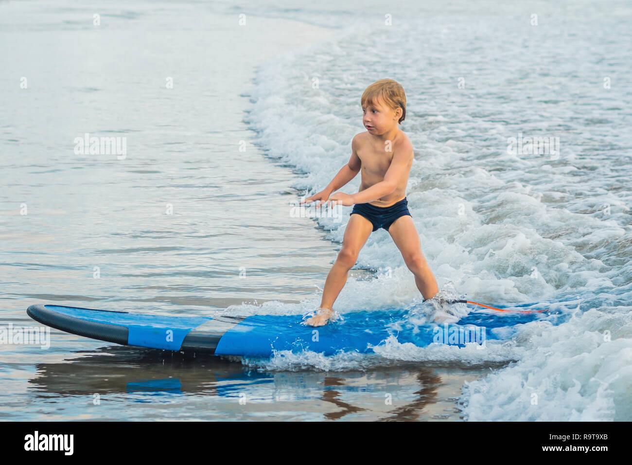 Little Boy surf sulla spiaggia tropicale. Bambino sulla tavola da surf sulle onde dell'oceano. Active sport acquatici per i bambini. Kid nuoto con il surf. Lezione di Surf per i bambini Foto Stock