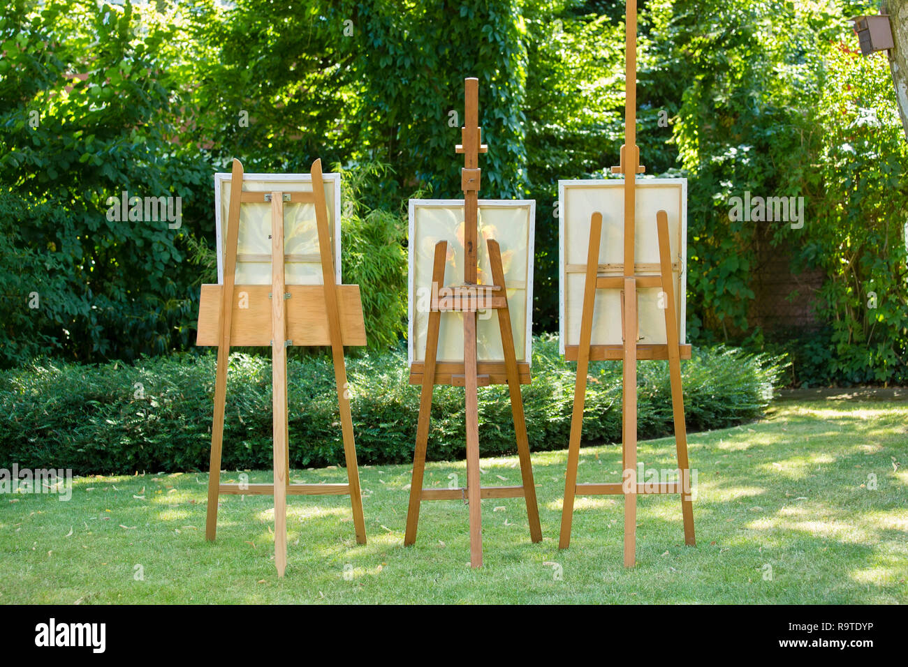 Tre cavalletti in legno con dipinti in piedi su un prato verde in un  ombroso giardino in un concetto di arte e natura Foto stock - Alamy