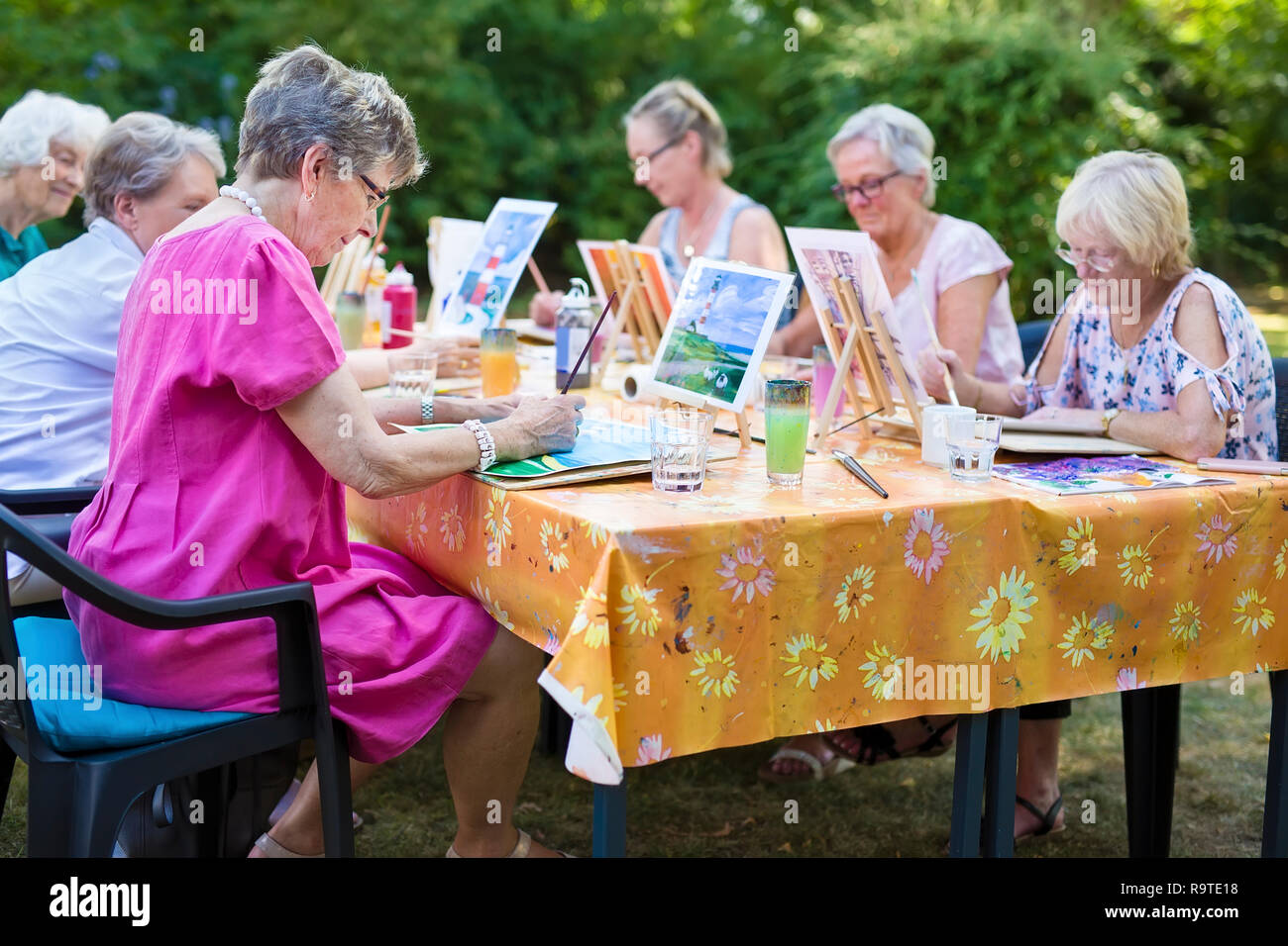 Il gruppo di donne senior prendendo lezioni di arte seduti all'aperto in corrispondenza di una tabella e di apprendimento insieme come dipingere immagini. Foto Stock