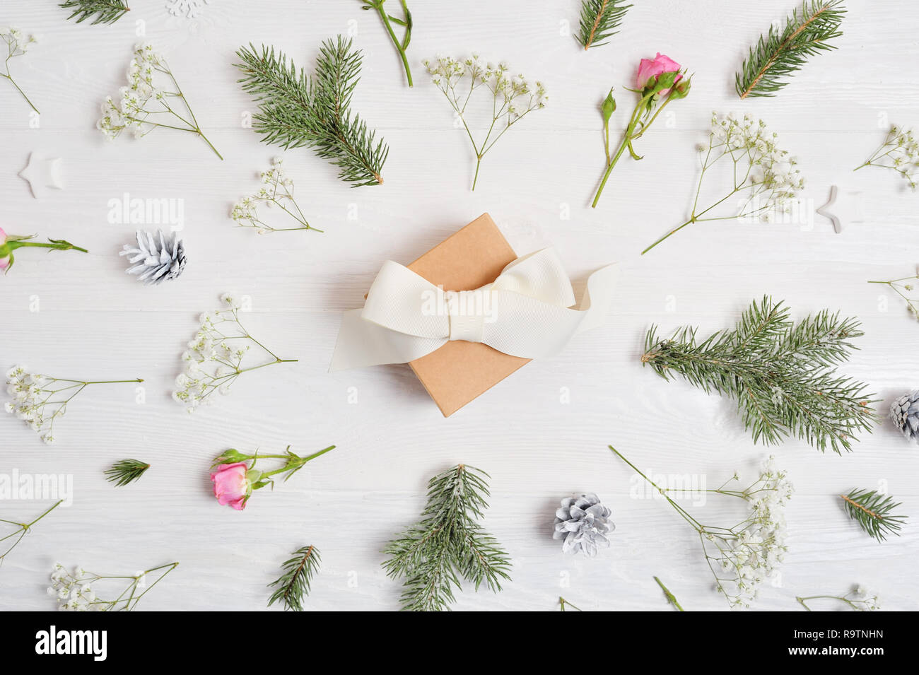 Abstract sfondo di Natale decorato con regalo in centro e xmas elementi - coni, rami di alberi, rose su un bianco sullo sfondo di legno Foto Stock
